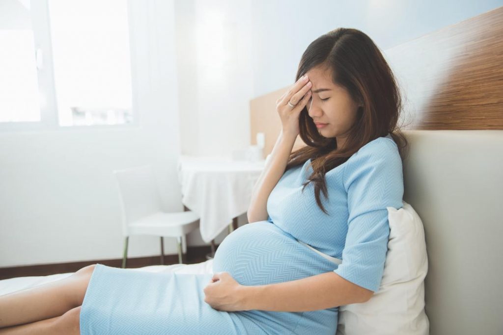 pregnant lady with a headache sits on bed low blood pressure